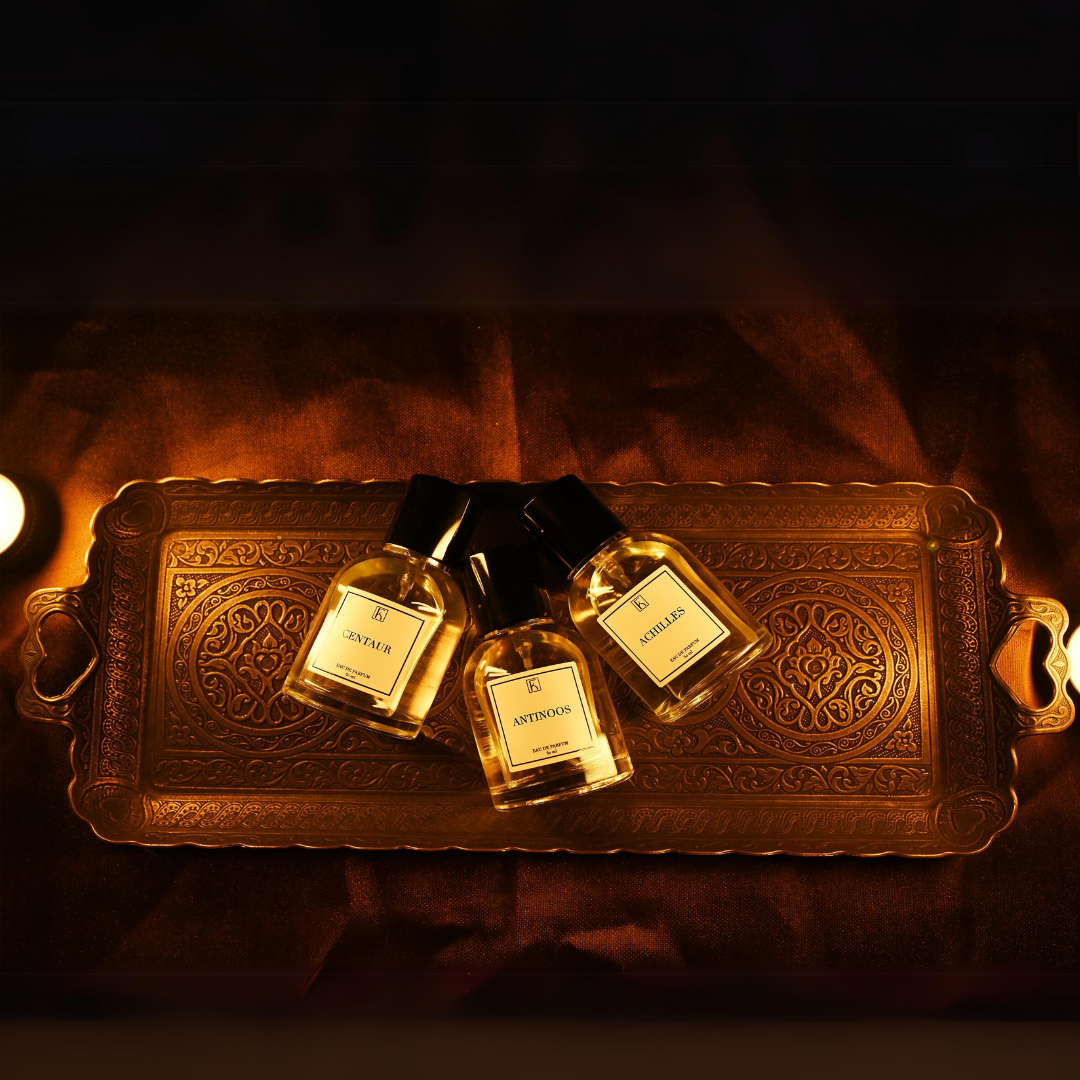 Auf einem reich verzierten goldenen Tablett liegen drei Parfümflaschen mit schwarzen Verschlüssen und weißen Etiketten.